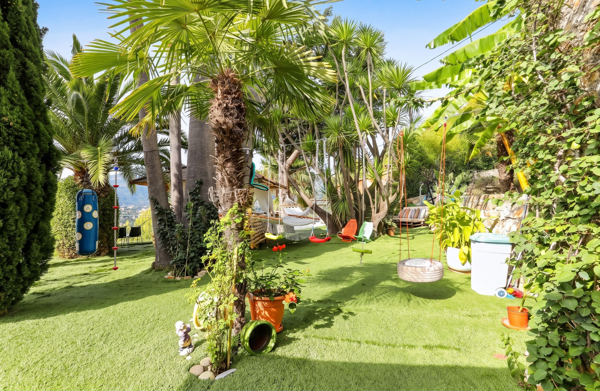 Un jardin luxuriant, avec des palmiers, un hamac et diverses plantes en pot.