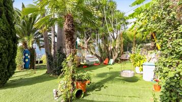 Un jardin luxuriant, avec des palmiers, un hamac et diverses plantes en pot.
