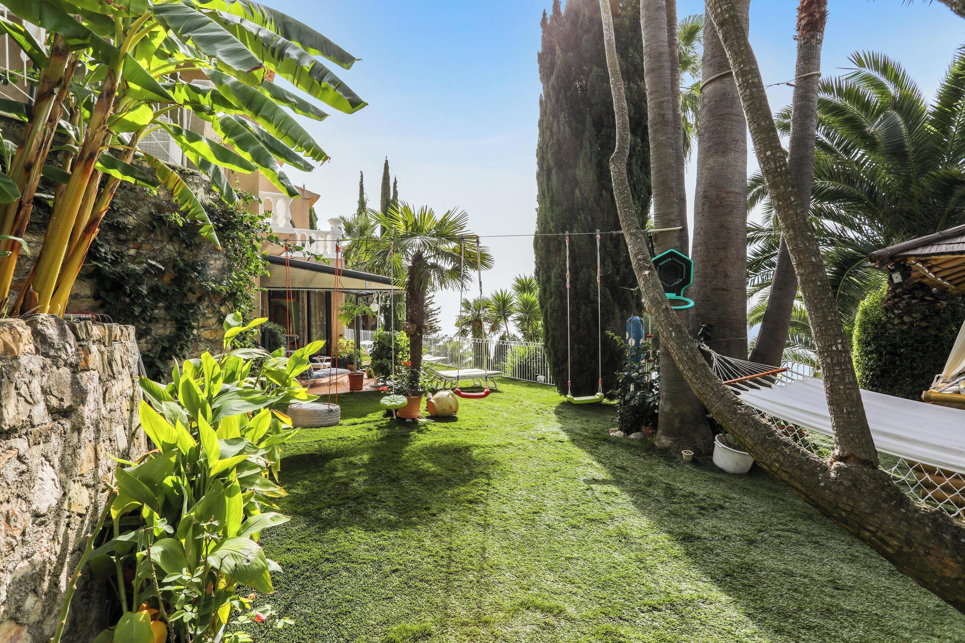 A well-maintained garden with a hammock, potted plants, and a stone wall.