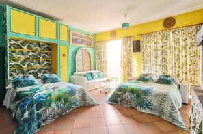 Una habitación con dos camas, un sofá blanco, una mesita y una ventana con cortinas.
