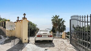 A white car parked at a gated entrance with a stone pathway, a metal fence, and a clear sky. - Homerez - Studio in Menton (Menton)
