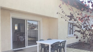 A patio with a white table and chairs, a sliding glass door, and a small window. - Single-Story House: Central Location, 150m from Beach, Terrace, Parking (Jullouville)