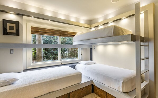 Une chambre avec un lit superposé, une fenêtre, un tableau encadré au mur et un plancher en bois.