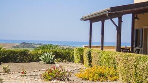 Vista costera con jardín al frente y un edificio con pérgola que domina el mar.