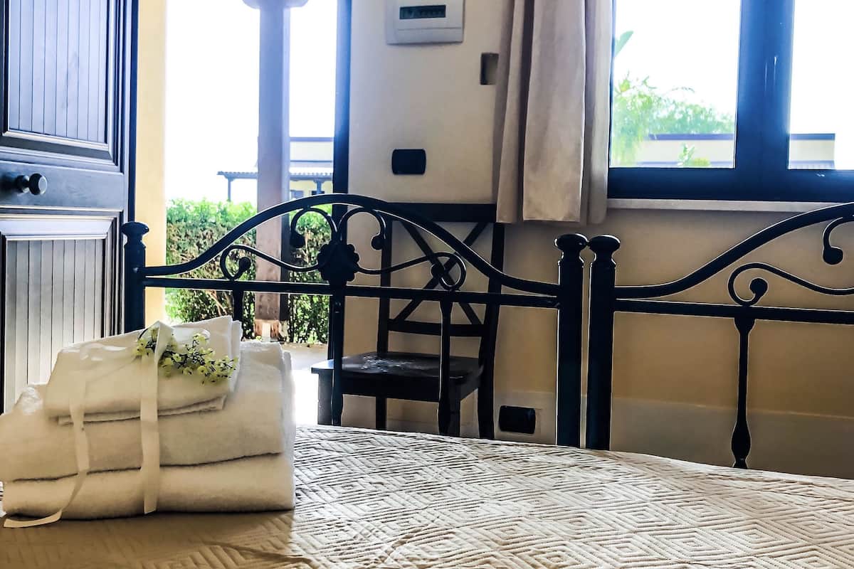 A bedroom with a bed, a chair, a window with curtains, and a view of the outdoors.