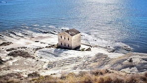 Un paisaje costero con un edificio de piedra cerca de la orilla, rodeado de formaciones rocosas blancas y el mar.