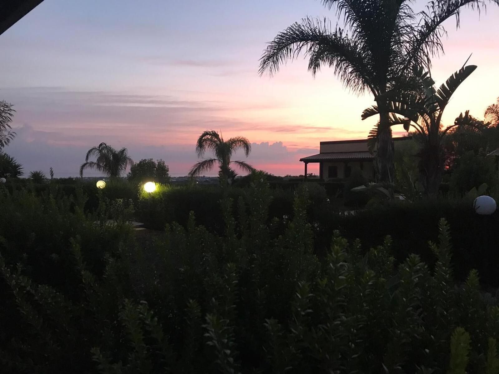 A sunset view with palm trees and a building in the foreground.