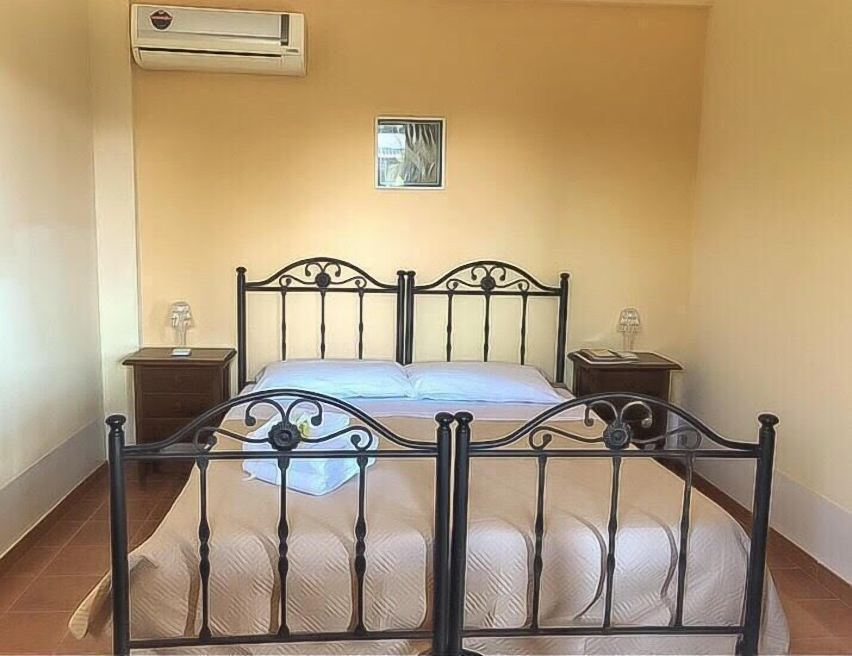 A bedroom with a bed, two bedside tables, an air conditioning unit, and a small picture on the wall.