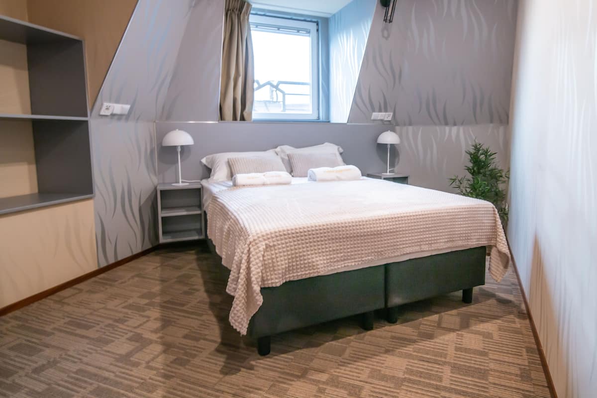 Un dormitorio con una cama, dos mesitas de noche, una ventana y una planta.
