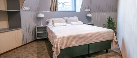 Un dormitorio con una cama, dos mesitas de noche, una ventana y una planta.