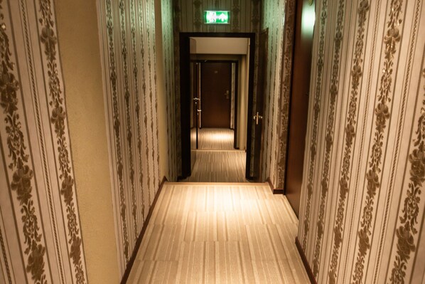 A narrow, carpeted hallway with patterned wallpaper and a door at the end.