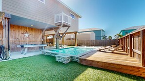 Un jardin avec une piscine, une terrasse en bois et un espace patio couvert.