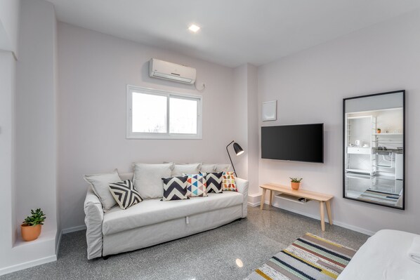 A modern living room with a sofa, a flat-screen TV, a bench, and a large mirror.