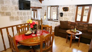 A dining area with a wooden table, chairs, and a red tablecloth. There is a flower vase on the table, and a small round table with a tray and a candle. - Apartments Zecic (Split)