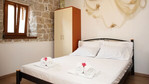 A bedroom with a stone wall, wooden wardrobe, and a bed with white linens and towels. - Apartments Zecic (Split)