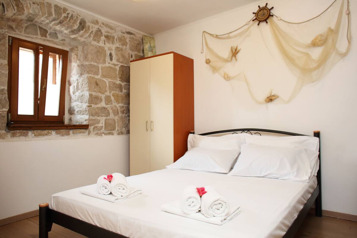 A bedroom with a stone wall, wooden wardrobe, and a bed with white linens and towels.