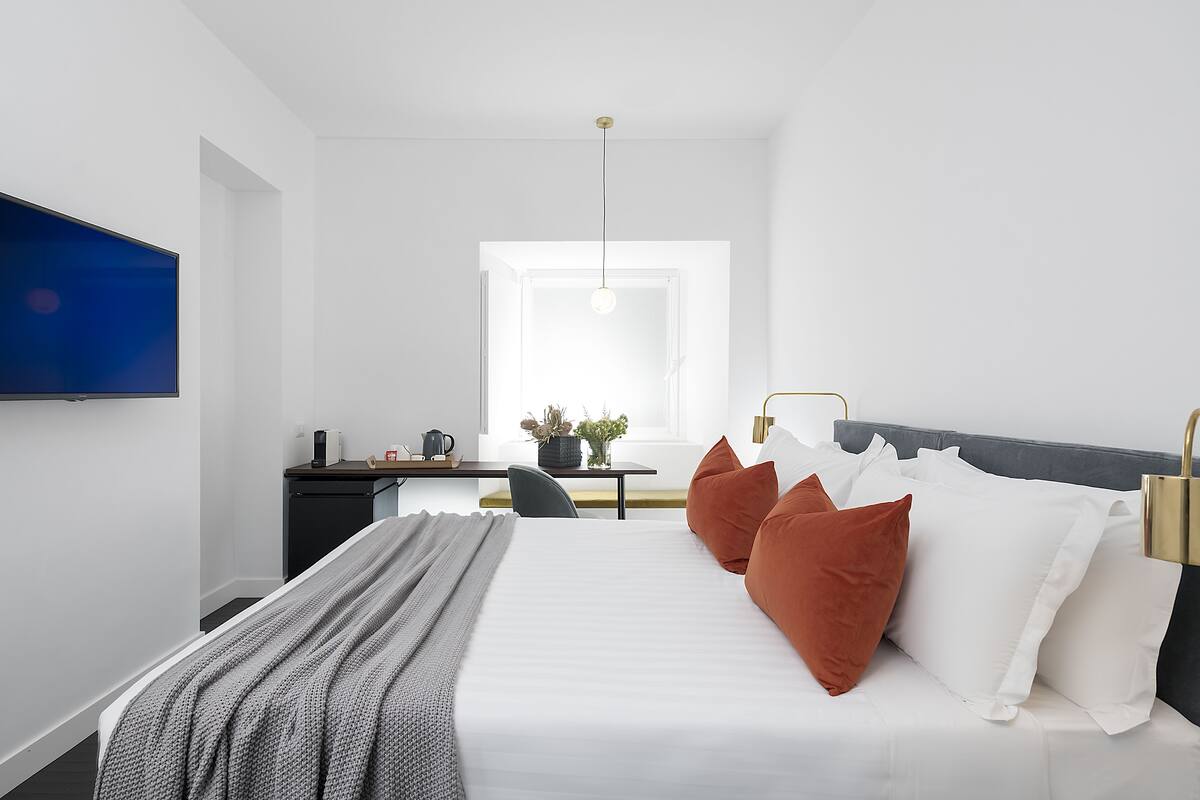 A modern bedroom with a large bed, a desk, a TV, and a window.