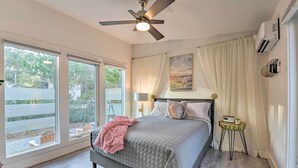 A bedroom with a bed, a ceiling fan, a window with blinds, a nightstand, and a painting on the wall.