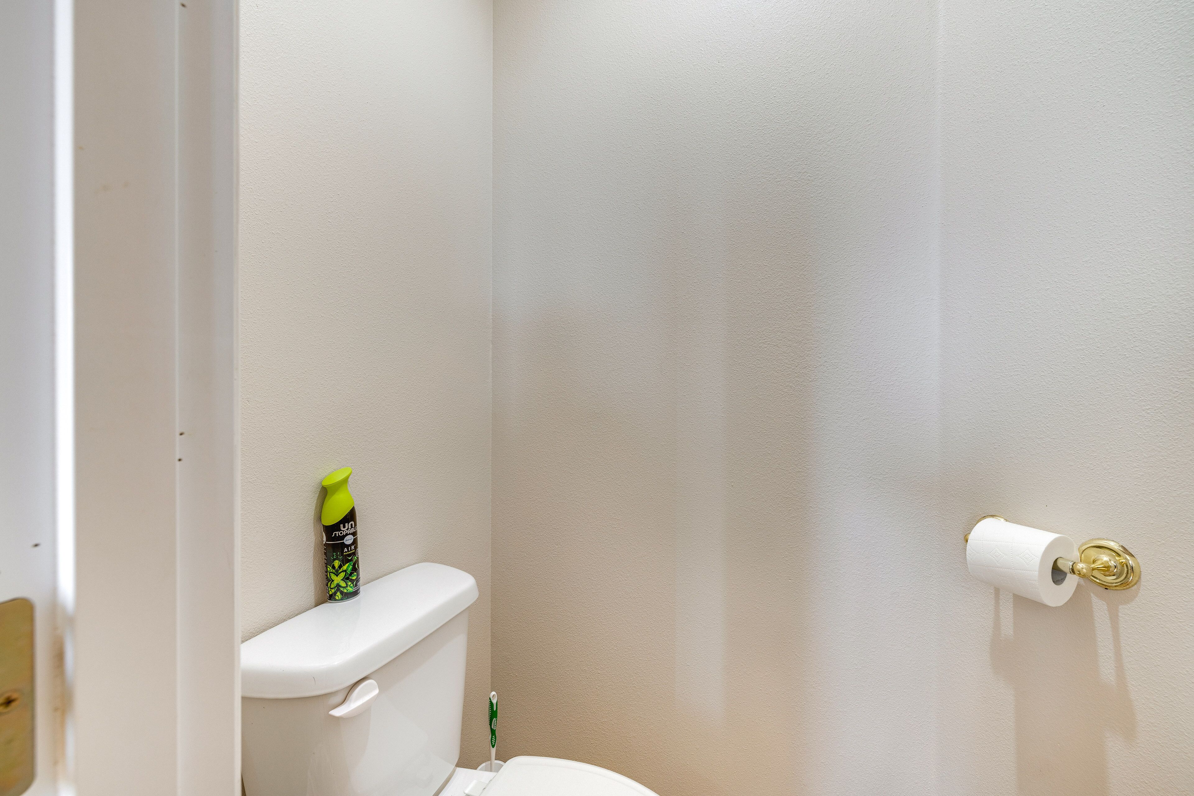 A bathroom with a toilet, a toilet paper holder, and a green bottle on the toilet tank.