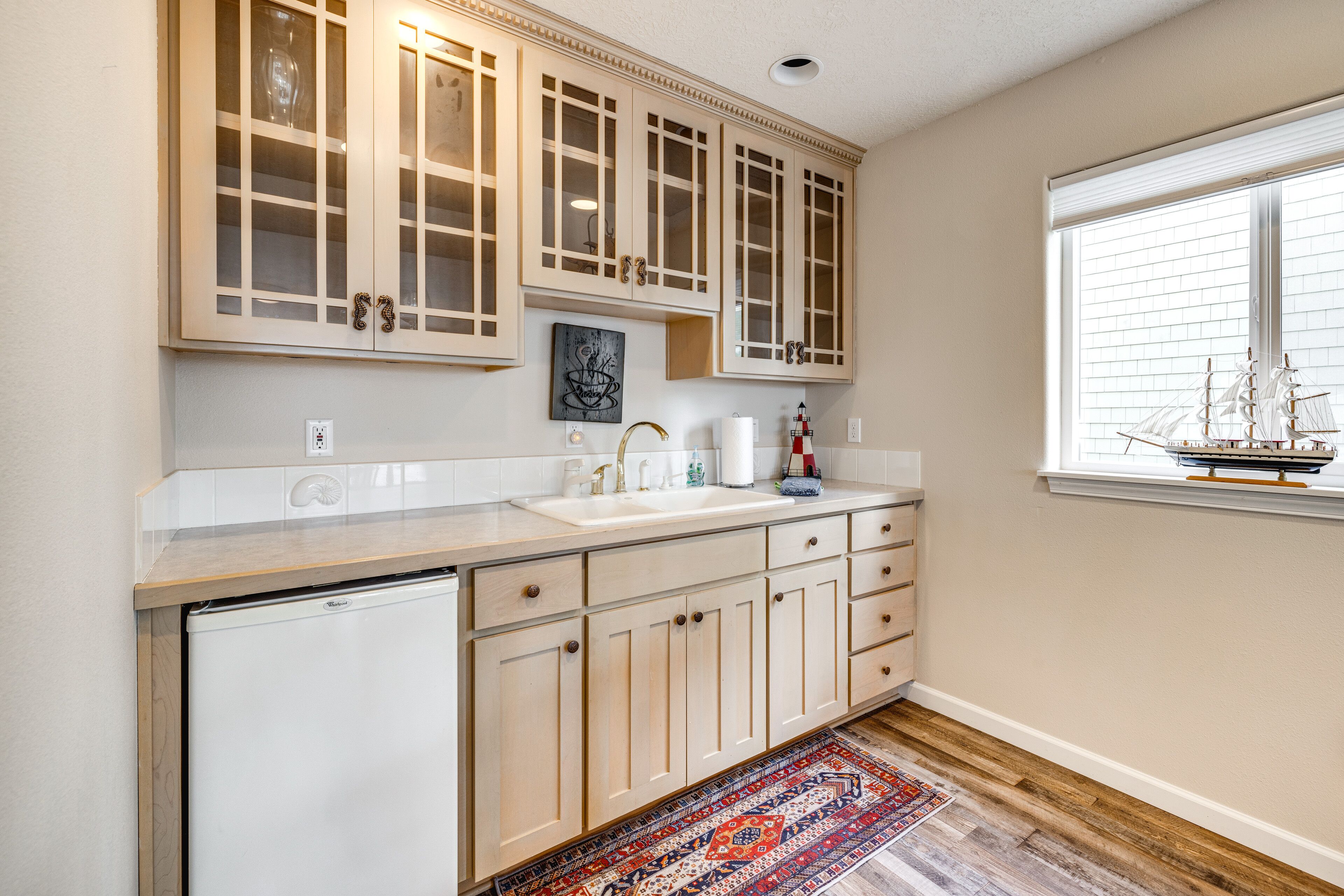 A kitchen with light wooden cabinets, a white countertop, a built-in dishwasher, and a window with blinds.