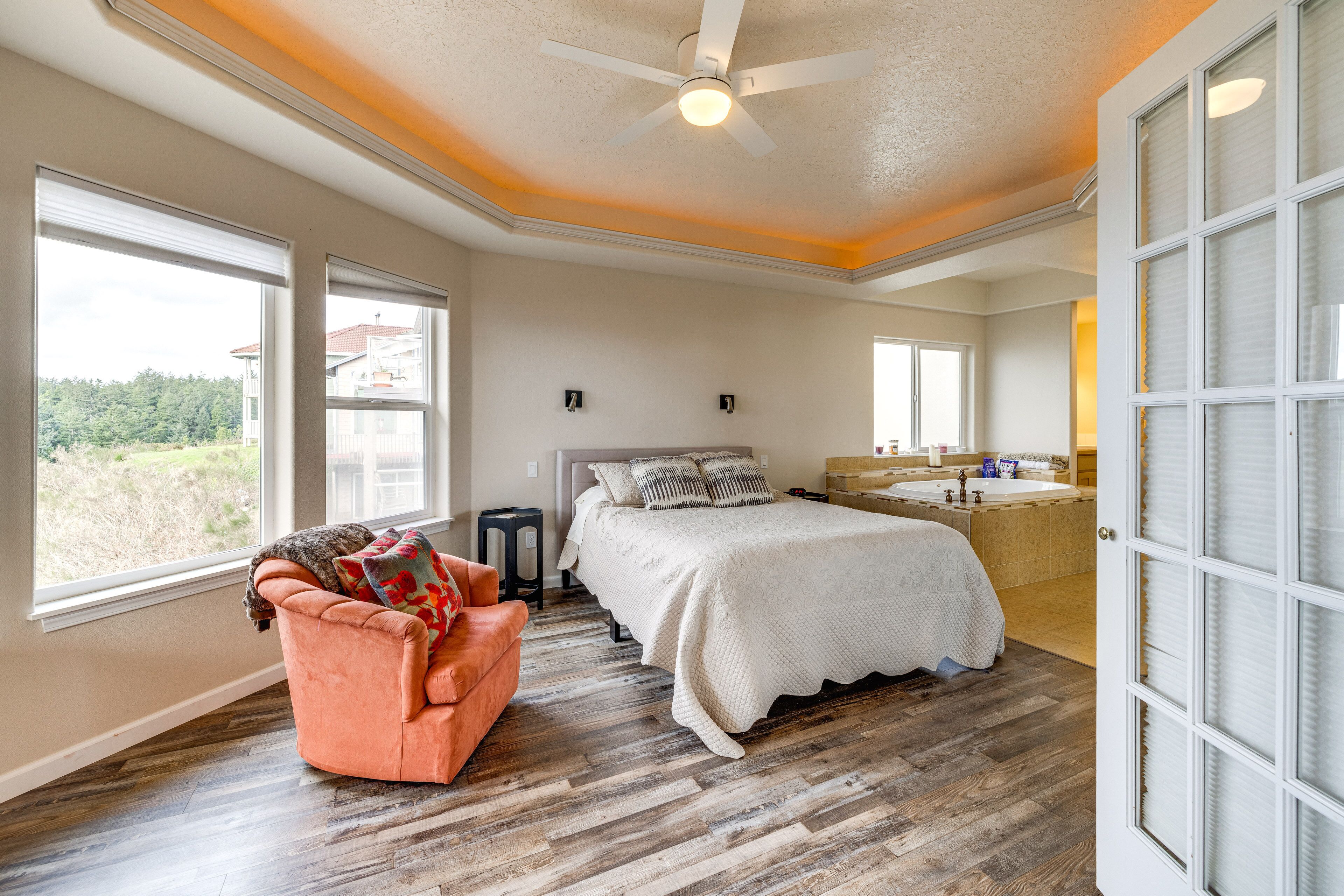A bedroom with a large bed, a chair, a ceiling fan, and a bathroom with a bathtub and sink.