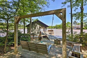 Une terrasse en bois avec une balançoire, un espace salon couvert et une vue sur un lac.