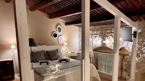 Un dormitorio con cama, lámparas de noche, una pared de piedra y televisión.