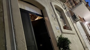 A building with a black door, a potted plant, and a window with bars. - Nonna Ninetta "typical Sicilian house" (Avola)