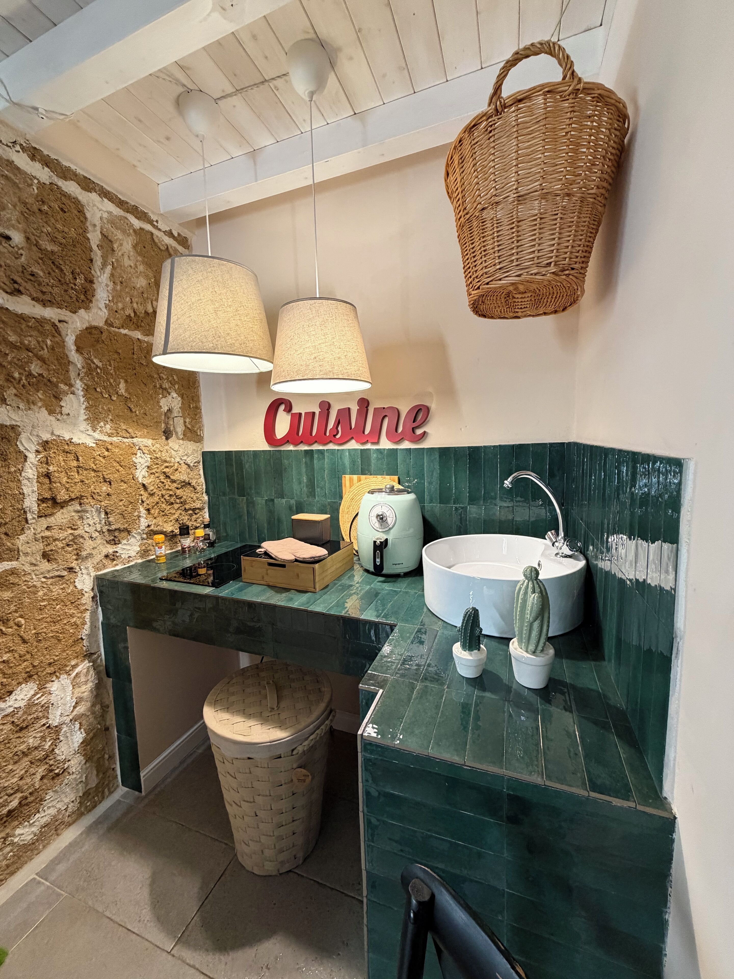 A kitchen with a stone wall, a green backsplash, a hanging basket, and a 'Cuisine' sign.