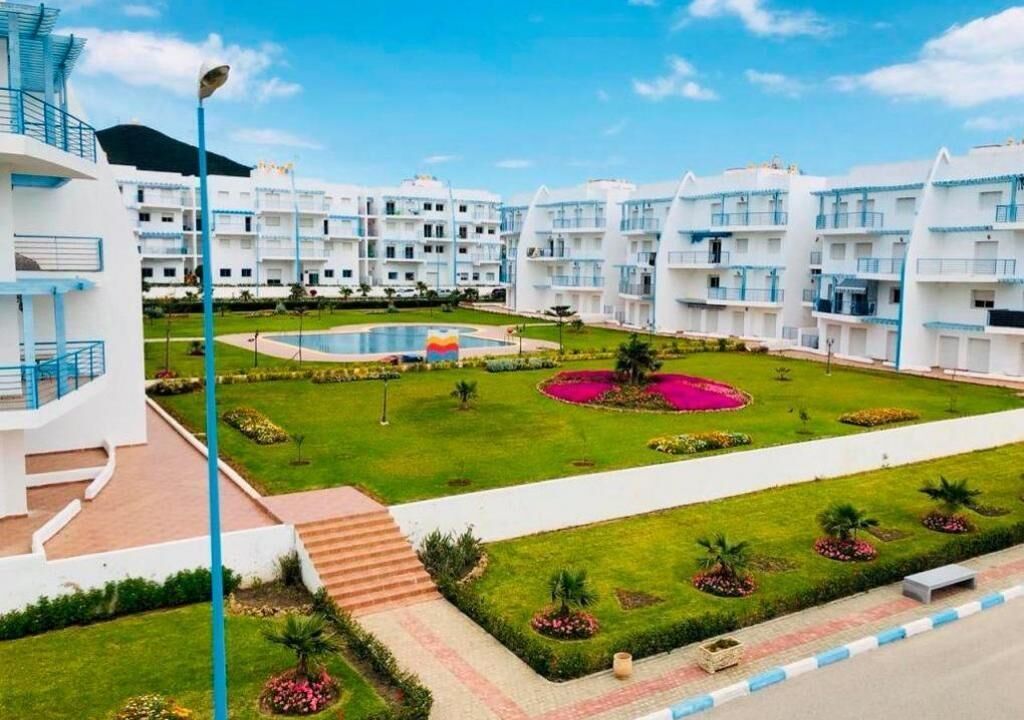 A modern hotel with multiple white buildings, a central pool, and well-maintained gardens.