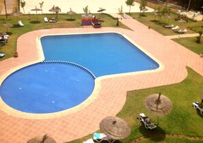 Una piscina con un deck circundante, sillas de descanso y sombrillas.
