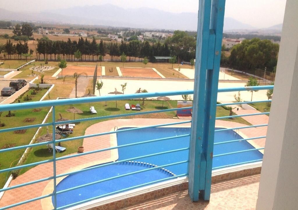 A view from a balcony overlooking a swimming pool, with a clear view of the surrounding landscape and distant mountains.