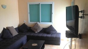 En stue med en mørk sofa, et lille sort sofabord og et fjernsyn ophængt på væggen.