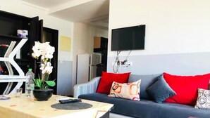Un salon avec un canapé, un téléviseur fixé au mur et une petite table sur laquelle se trouve une télécommande.