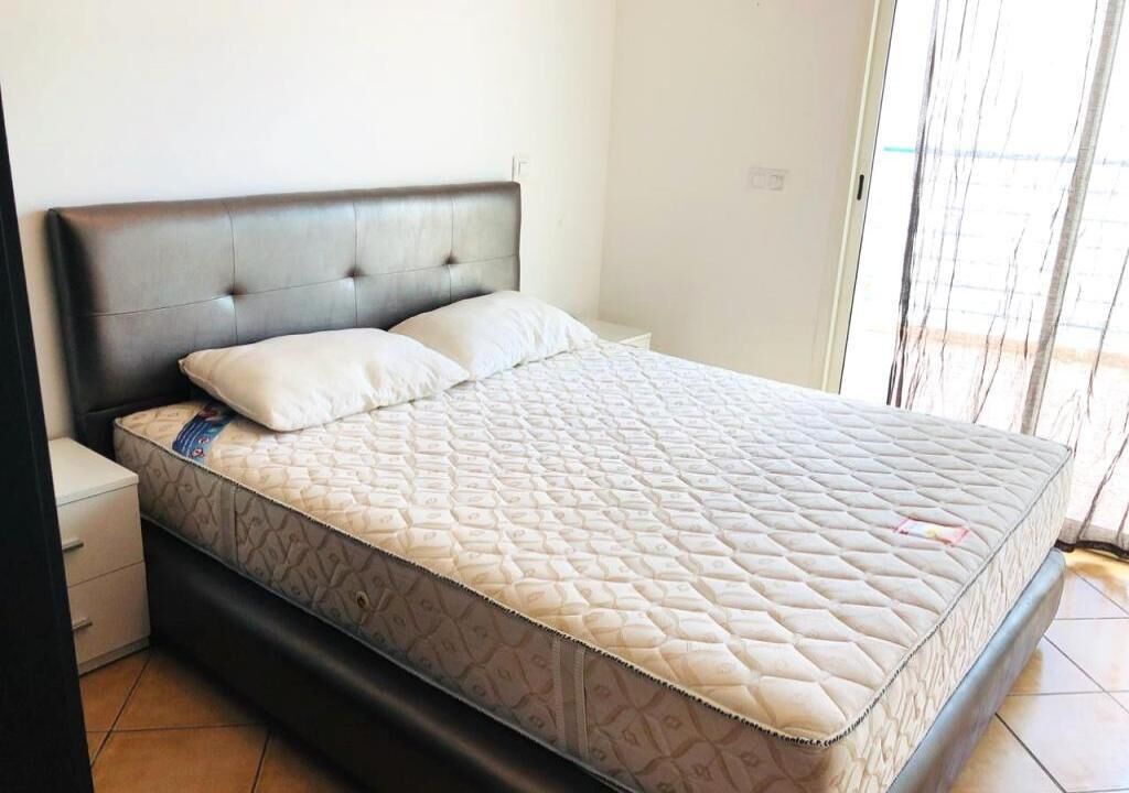 A single-bed room with a dark headboard, a white mattress, and a small bedside table.