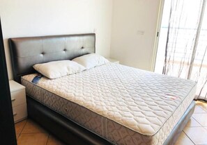 A single-bed room with a dark headboard, a white mattress, and a small bedside table. - Residence Riviera Beach 4117 (Cabo Negro)
