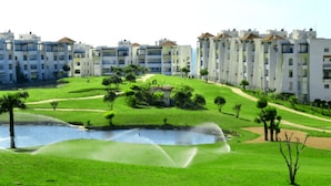 A residential area with modern apartment buildings, a well-maintained lawn, and a small pond with a fountain. - Beautiful apartment pool view in Marina Asilah 3923 (Asilah)