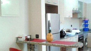 A kitchen with a granite countertop, red chairs, a refrigerator, a stove, and a washing machine. - Beautiful apartment pool view in Marina Asilah 3923 (Asilah)
