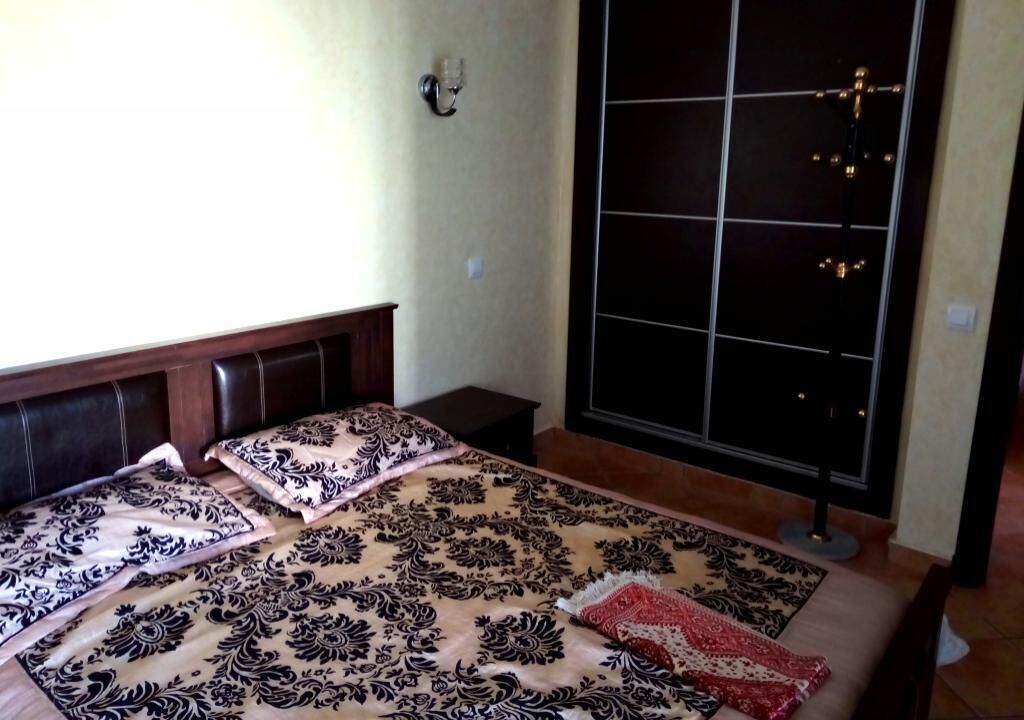 Une chambre à coucher avec un grand lit, une table de chevet, une fenêtre à carreaux et un luminaire fixé au mur.