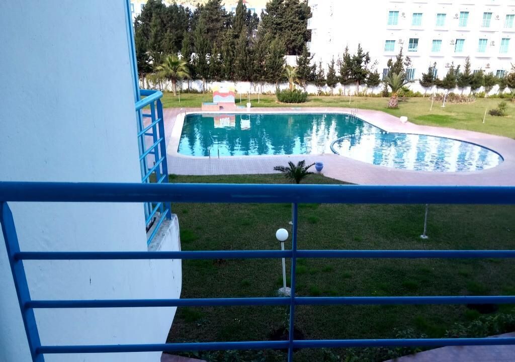 A swimming pool with a curved edge, surrounded by a grassy area and trees.
