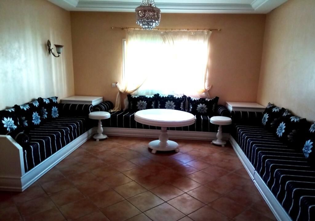 A room with a round table and two white chairs in the center, surrounded by black and white patterned sofas.