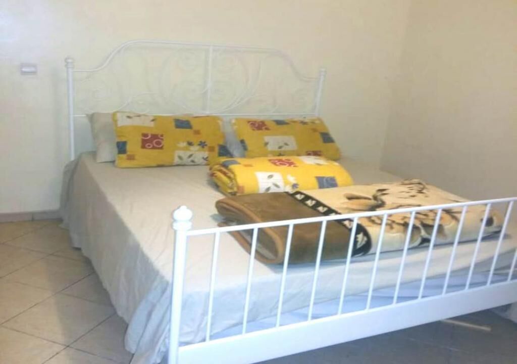 Un llit amb estructura metàl·lica blanca, matalàs beix i dos coixins grocs amb dibuixos.