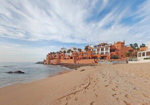 A beachfront property with a series of buildings along the shore, a sandy beach, and the ocean in the background. - Pool view apartment in Bouznika 3964 (Bouznika)