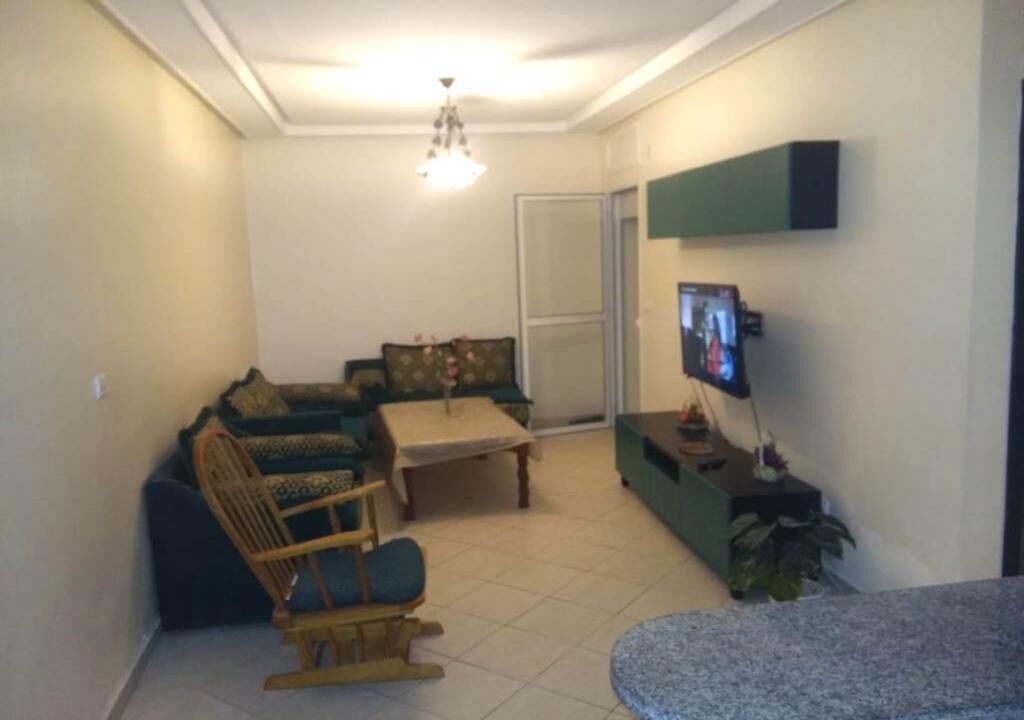 A living room with a sofa, a rocking chair, a coffee table, and a television mounted on the wall.
