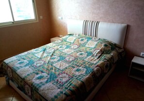 Ein Schlafzimmer mit einem Bett, einem Nachttisch, einem Fenster und einer Steckdose.