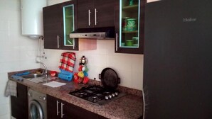 A compact kitchen with dark wooden cabinets, a gas stove, a washing machine, and a refrigerator. - Residence Riviera Beach 4110 (Cabo Negro)