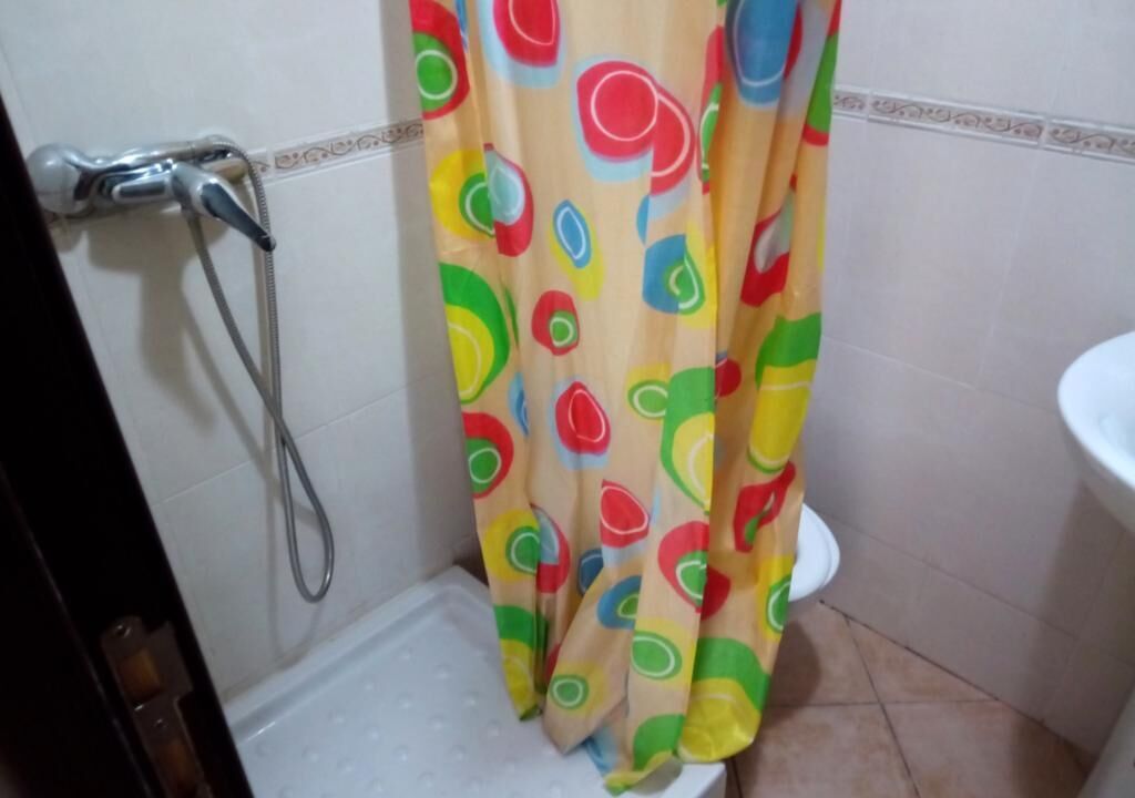 Ein Badezimmer mit Duschvorhang mit farbigem, abstraktem Muster, einer weißen Toilette und einem Duschkopf.