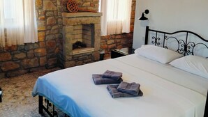 Un dormitorio con chimenea de piedra, una cama con ropa de cama blanca y una mesita de noche con lámpara.
