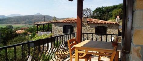 A balcony with a table and chairs, overlooking a mountainous landscape.