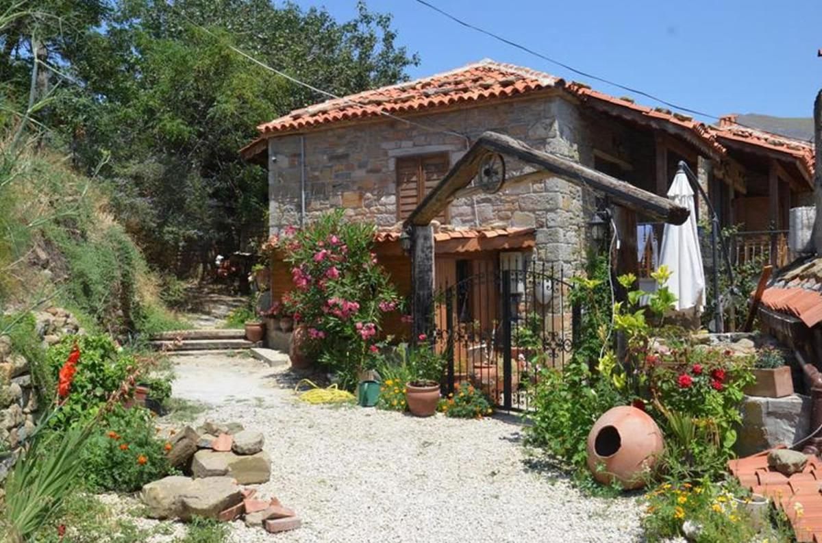 A stone house with a tiled roof, a gravel pathway, and potted plants.